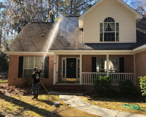 A person is using an air hose to clean the roof of a house.