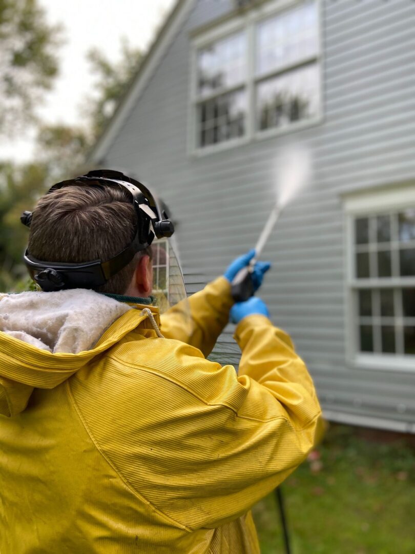 A man spraying water on the outside of a house.