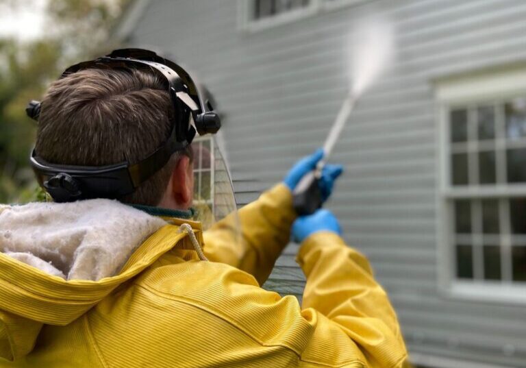 A man spraying water on the outside of a house.